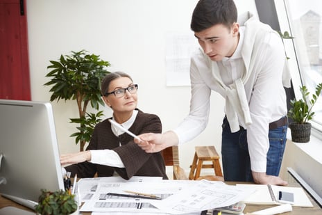 team-of-two-skillful-architects-young-man-and-elderly-woman-developing-new-residential-housing-project-working-on-generic-computer-in-office-using-cad-program-man-pointing-at-screen-with-pencil